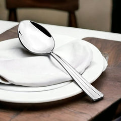 FNS Venice stainless steel serving spoon displayed on white plate with napkin in elegant dining table setting