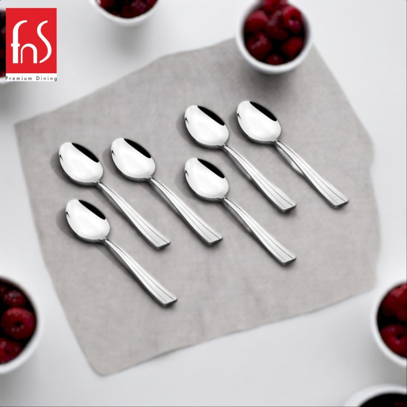 Six polished stainless steel Venice teaspoons with ribbed handles arranged on gray square plate, surrounded by white bowls of red berries at corners, FnS Premium Dining logo visible