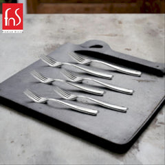 Six stainless steel dinner forks arranged on gray slate board, marble countertop background, FnS Premium Dining branding visible.