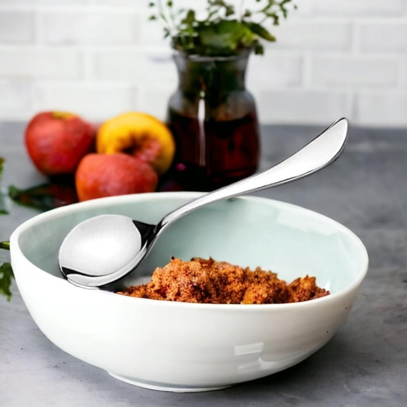 FNS Victoria serving spoon placed in white bowl with dessert on gray counter, with fresh fruits and herb vase creating elegant kitchen lifestyle setting.