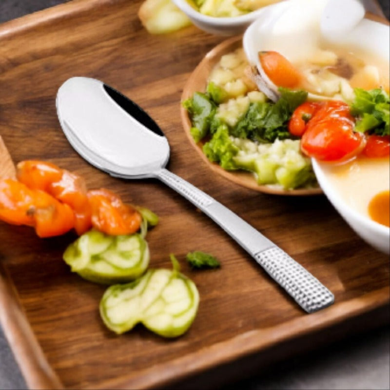 FNS Zest large serving spoon displayed on wooden board with fresh vegetables, cherry tomatoes, and cucumber slices in premium dining setup.