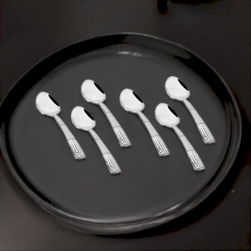 Overhead view of six stainless steel teaspoons with textured handles arranged on a dark circular tray in Premium Dining presentation.