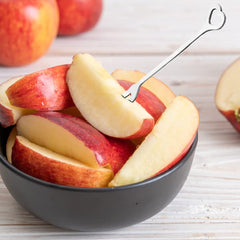 Apple slices in dark bowl with heart-shaped fork, whole apples nearby