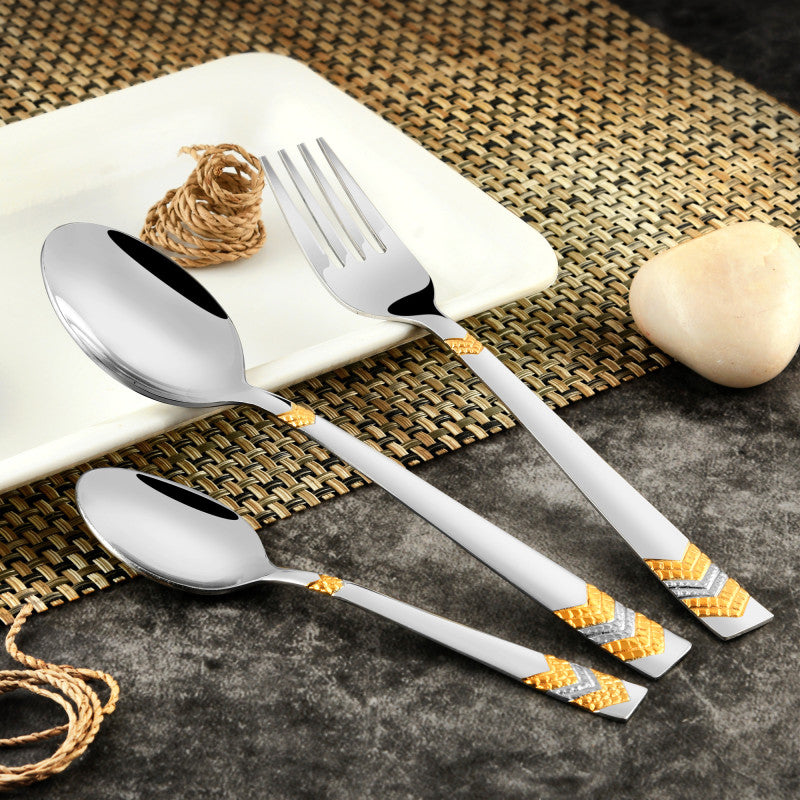 Elegant fork and spoons with chevron gold handles set beside plate on a decorative woven mat.