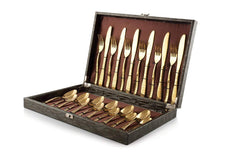 Luxury gold cutlery set displayed in open box with floral decoration and ribbon on marble surface.