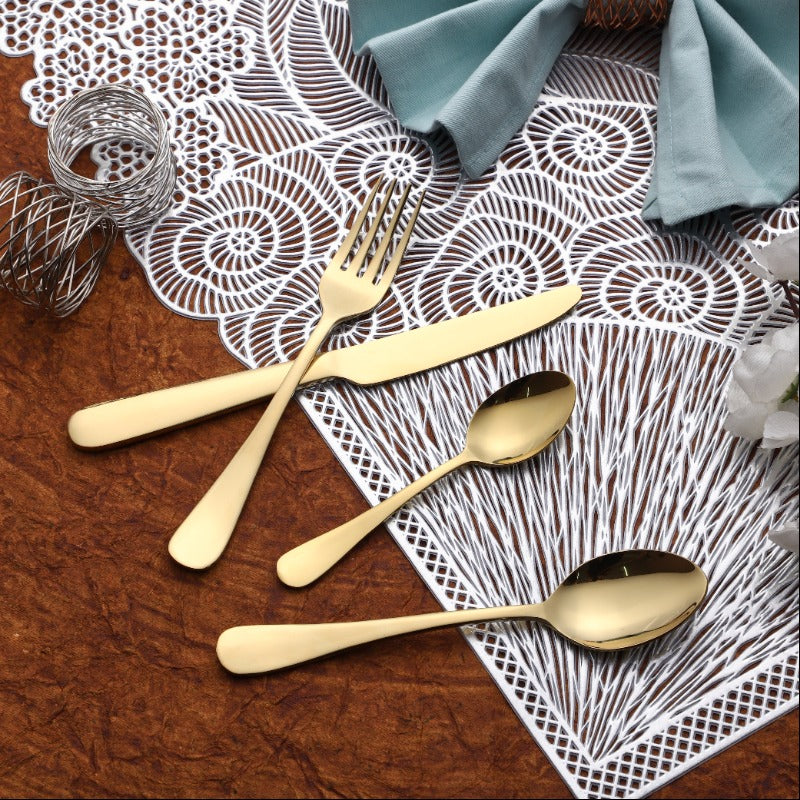 Gold cutlery set arranged on decorative white placemat with teal napkin and metallic napkin ring.