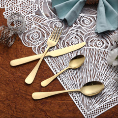 Gold cutlery set arranged on decorative white placemat with teal napkin and metallic napkin ring.