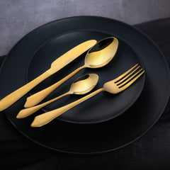 Modern gold flatware set displayed stylishly on matte black dinner plates with a dark background.