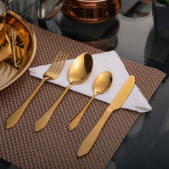 Gold cutlery placed on folded white napkin, set on woven brown placemat near copper serveware.