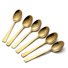 Six gold dessert spoons arranged in diagonal overlapping pattern showing mirror finish on white background