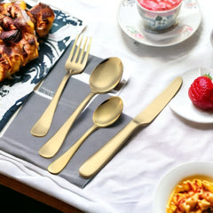 Four-piece golden cutlery set displayed beside plated desserts and dishes on a white dining table.
