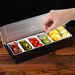 Hand with fork reaching into condiment caddy filled with red grapes, green olives, cherry tomatoes, kiwi, and orange slices on wooden surface