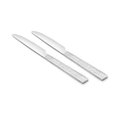 Pair of FnS Helios stainless steel dinner knives with distinctive perforated rectangular handles arranged diagonally on white background.