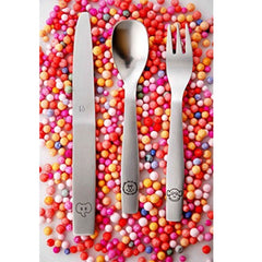 Children’s cutlery set with engraved animal handles placed on vibrant, colorful candy sprinkles background.