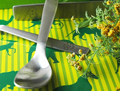 Close-up of spoon and knife with engraved animals on jungle-themed yellow and green striped background.