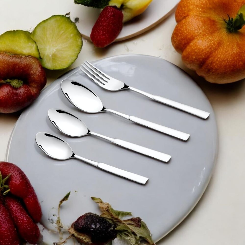 Shiny cutlery placed on a gray plate, surrounded by fresh fruits on a white table.