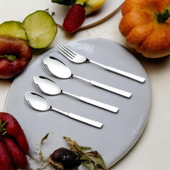 Shiny cutlery placed on a gray plate, surrounded by fresh fruits on a white table.