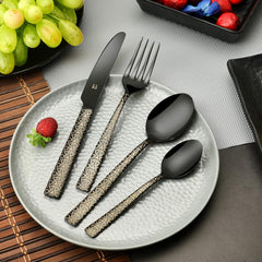 Stylish black cutlery set with gold-accented pattern on a grey plate, surrounded by grapes and berries.