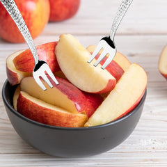 Apple slices in dark bowl with two decorative forks inserted