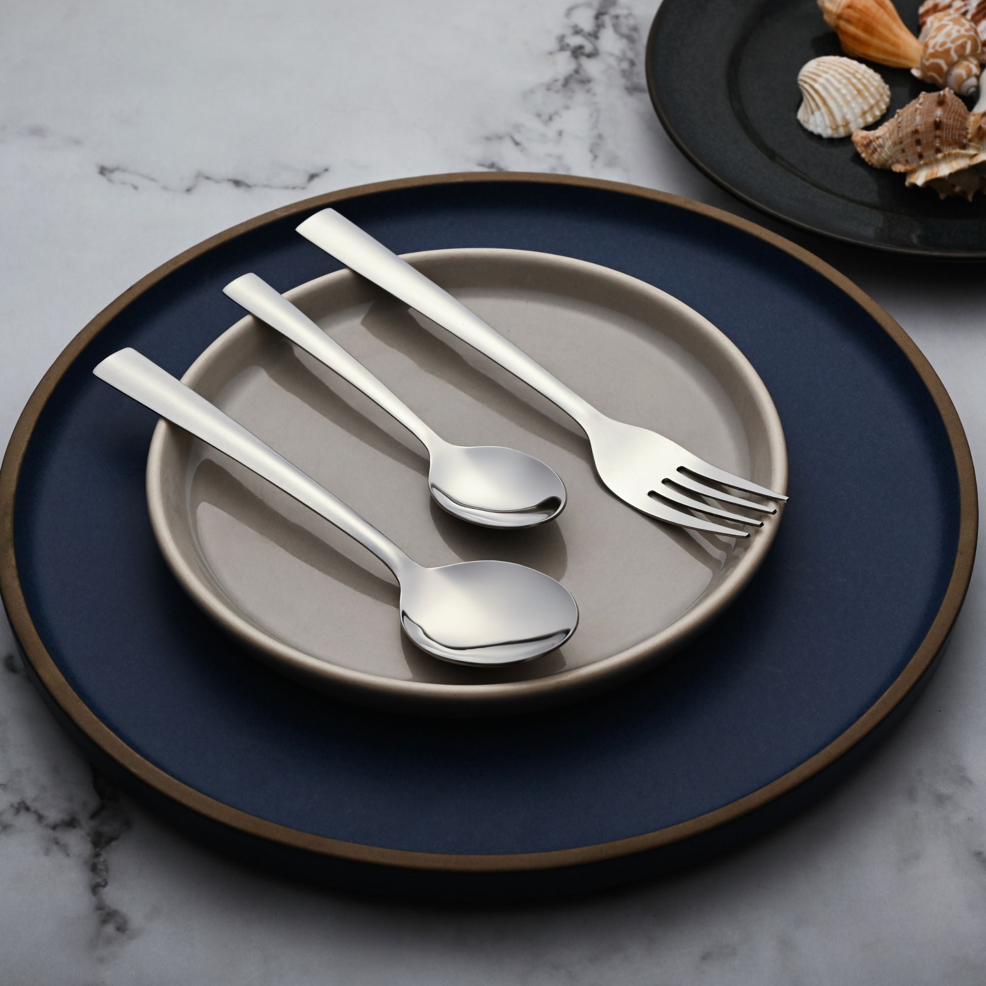 Three-piece cutlery set with wide handles placed elegantly on stacked beige and navy ceramic plates.