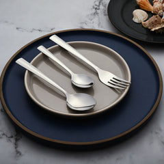Three-piece cutlery set with wide handles placed elegantly on stacked beige and navy ceramic plates.