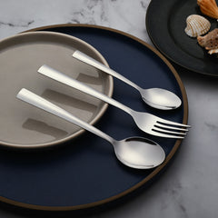 Modern cutlery set with flat handles displayed beside plates on a marble surface with seashell decor.
