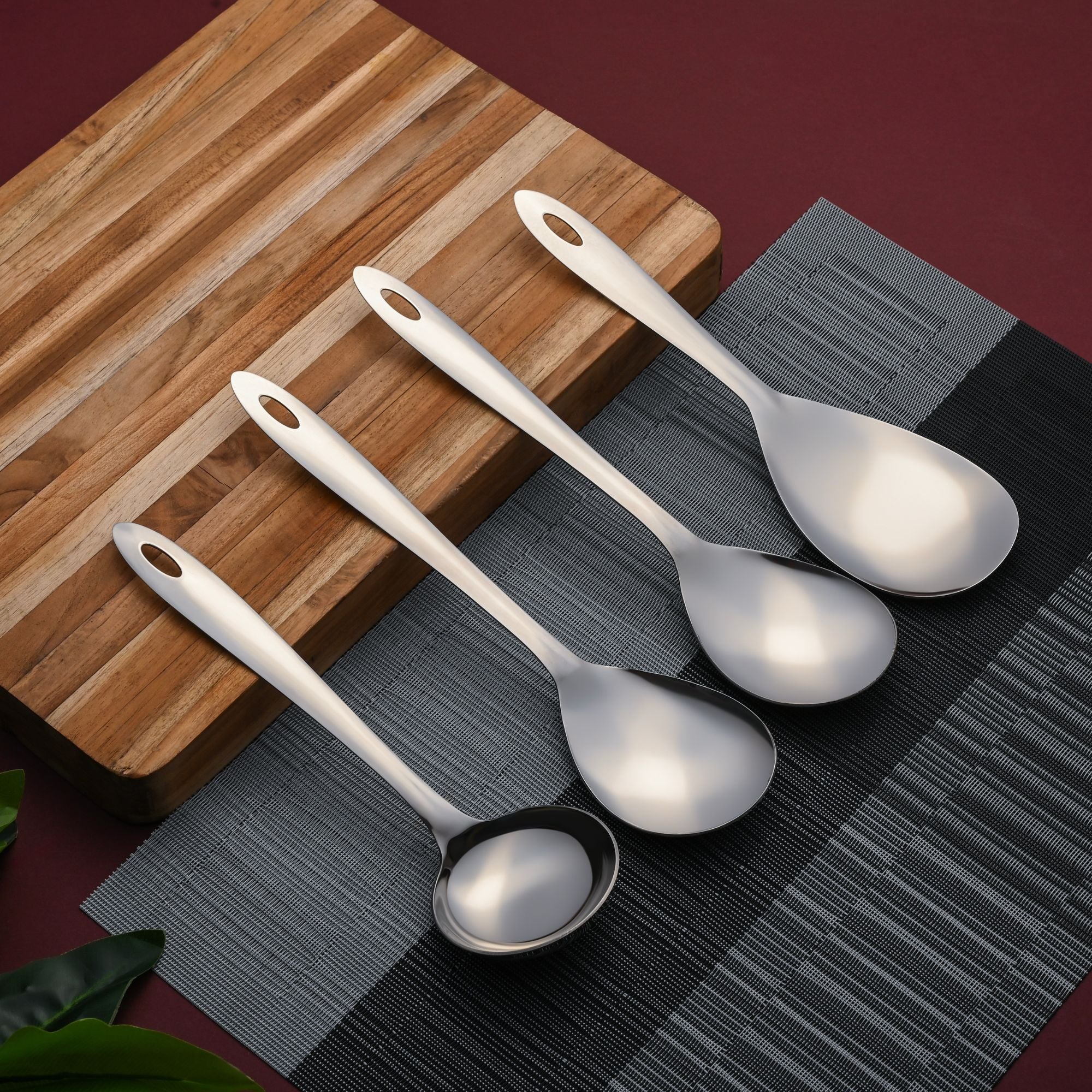 Montavo Amazon 4-piece stainless steel serving spoons on striped wooden board with black placemat, showcasing mirror polish finish and ergonomic design.