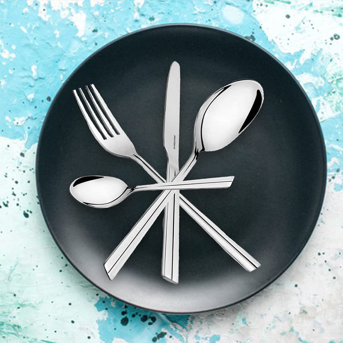 Modern stainless steel flatware set arranged star-style on matte black plate with artistic blue background.