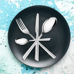 Modern stainless steel flatware set arranged star-style on matte black plate with artistic blue background.