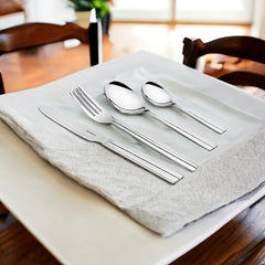 Elegant flatware set placed on folded napkin over ceramic plate in bright, cozy dining room setup.