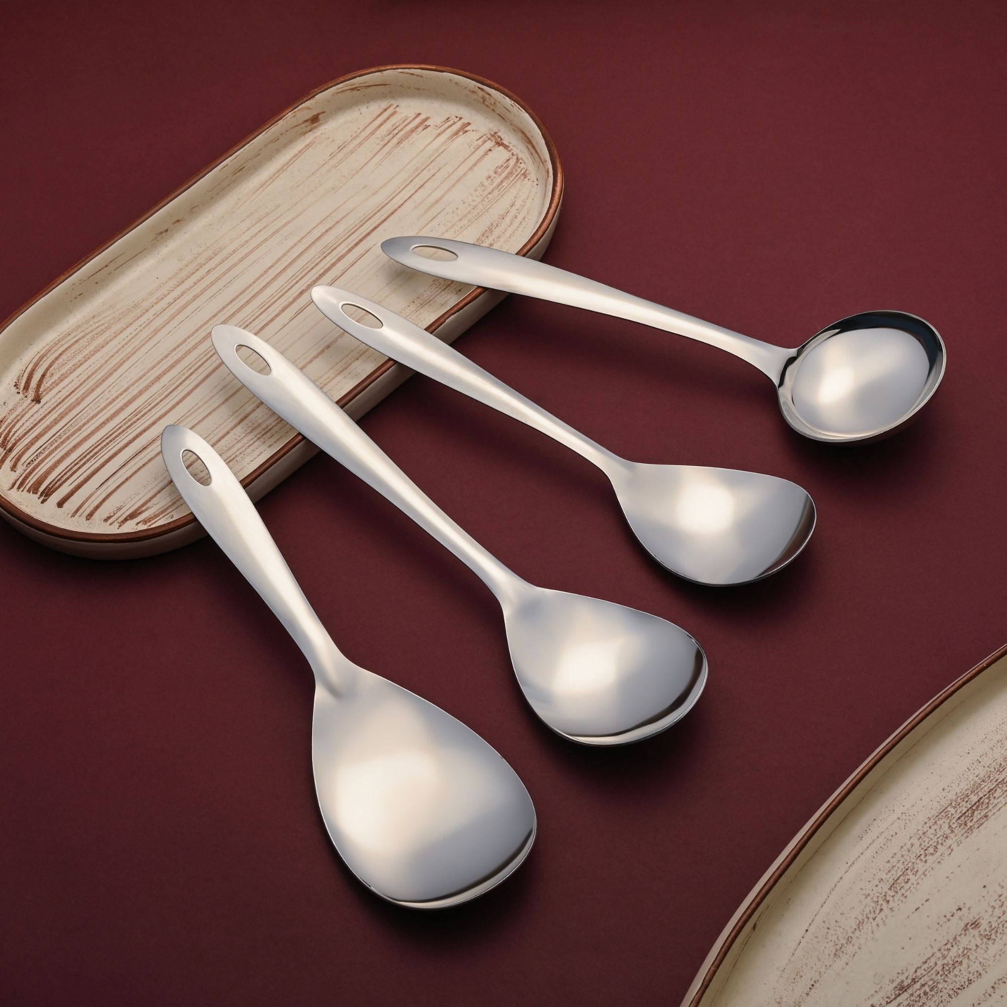 Premium Montavo stainless steel serving spoons set arranged elegantly with wooden coaster on burgundy textured background.