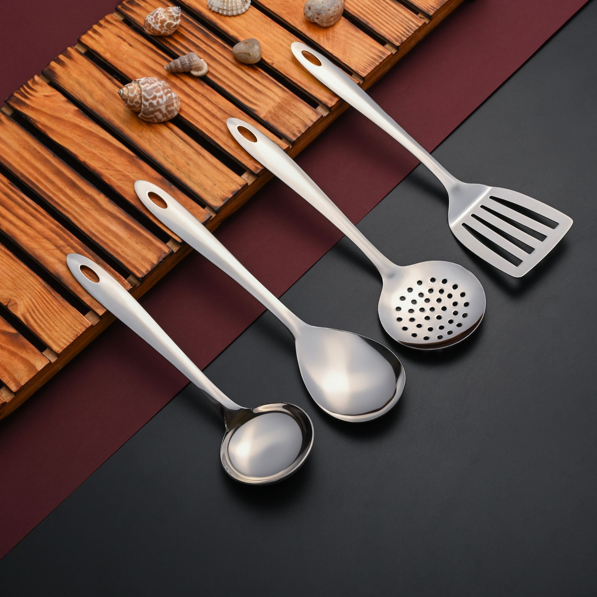 Montavo serving tools kitchen essentials set displayed on wooden surface with decorative seashells and burgundy background.