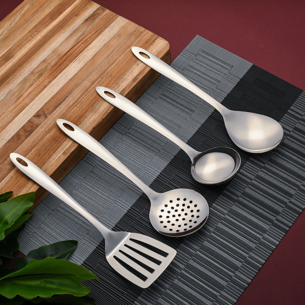 Elegant Montavo stainless steel serving tools arranged on textured kitchen linens with wooden coaster and plant styling.
