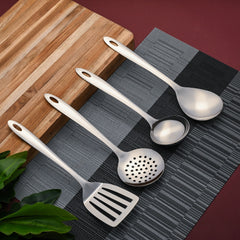 Elegant Montavo stainless steel serving tools arranged on textured kitchen linens with wooden coaster and plant styling.