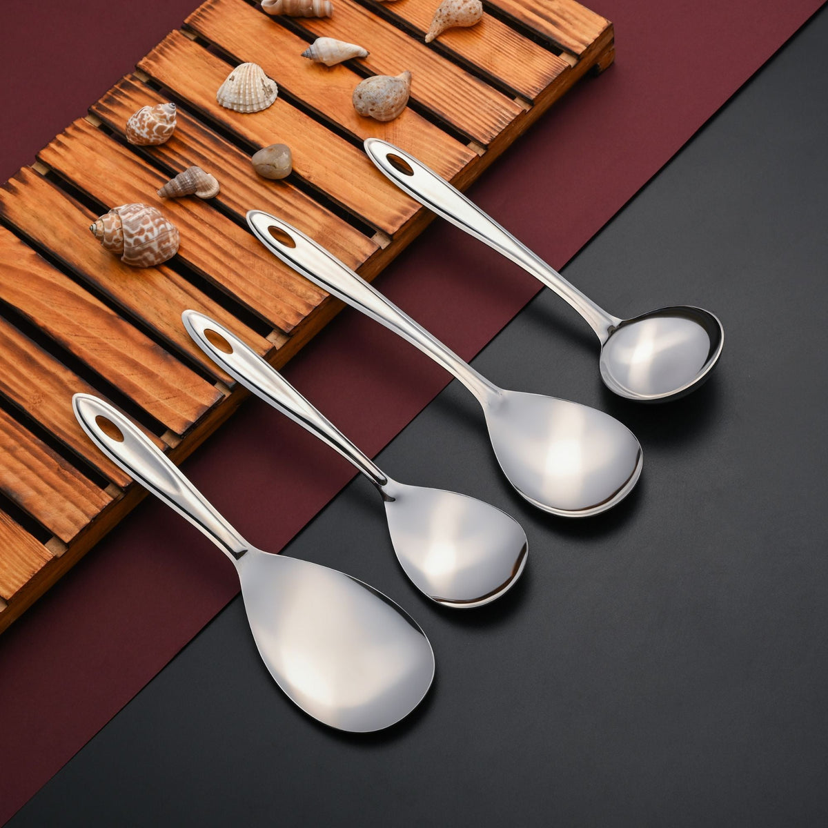 Trinity serving spoons stylized on wooden board with decorative seashells, burgundy and grey background with professional product photography.