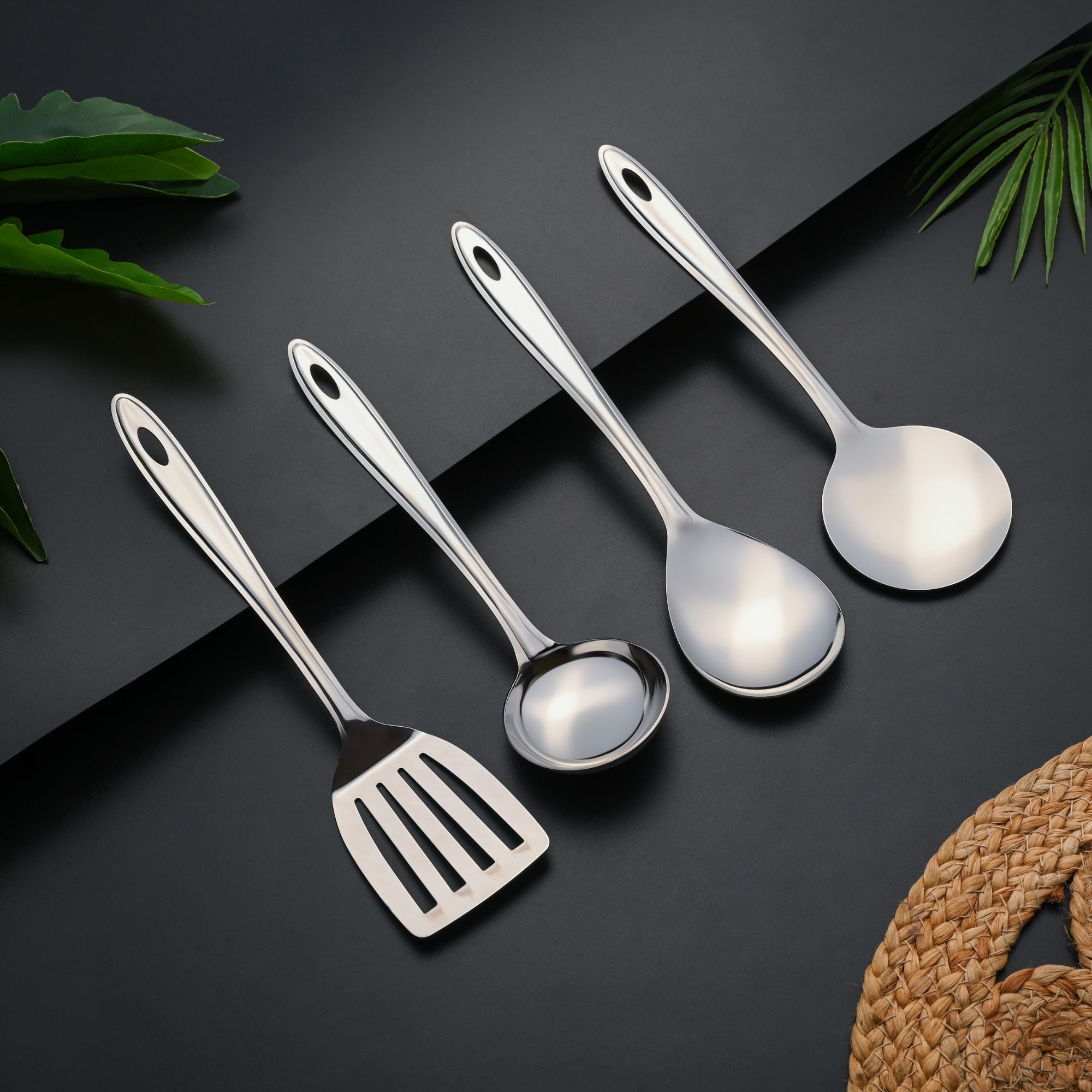 Montavo Trinity stainless steel serving tools set of 4 arranged diagonally on dark surface with green plant accents