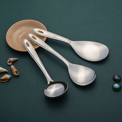 Trinity serving spoons displayed on teal background with decorative wooden plate and seashells for elegant product photography styling.