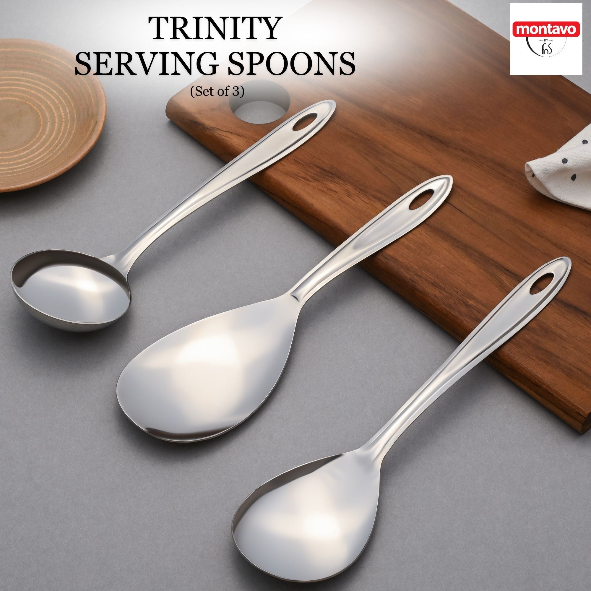 Set of three montavo trinity stainless steel serving spoons with elongated handles displayed on wooden surface and grey background.