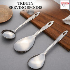Set of three montavo trinity stainless steel serving spoons with elongated handles displayed on wooden surface and grey background.