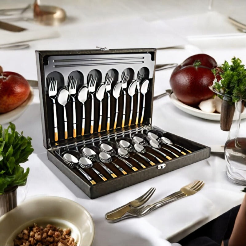 Elegant gold-handled cutlery set in open display box on white-table dining setup with fruits and dishes.