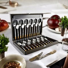 Elegant gold-handled cutlery set in open display box on white-table dining setup with fruits and dishes.