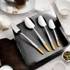 Sophisticated cutlery set with gold handles displayed elegantly on a black tray with coffee and snacks.