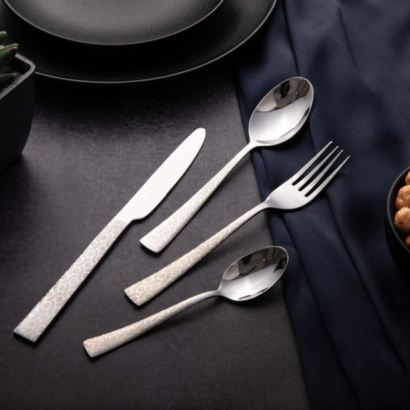 Stylish cutlery set with engraved handles placed beside black dinnerware on a dark textured surface.