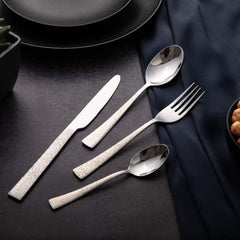 Stylish cutlery set with engraved handles placed beside black dinnerware on a dark textured surface.