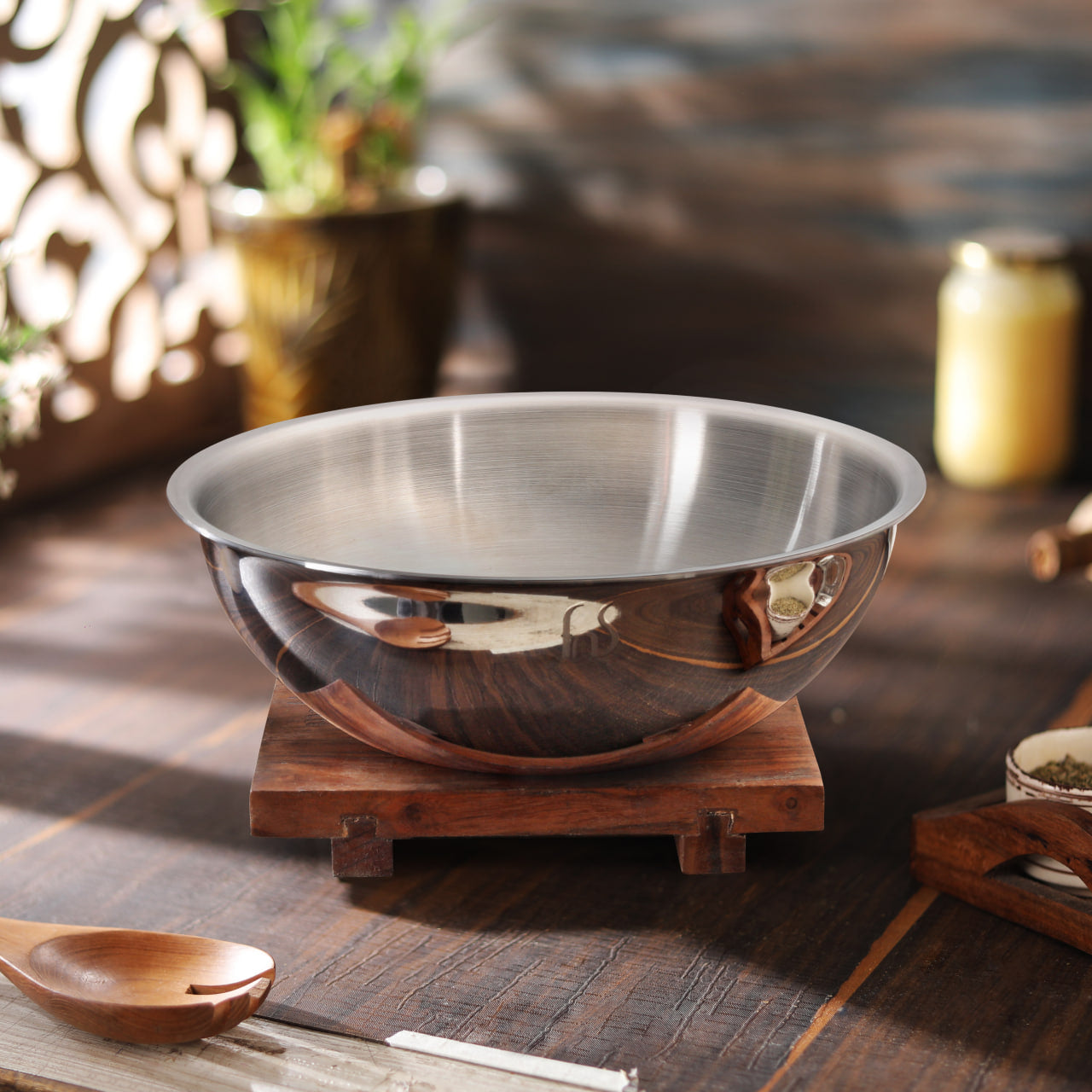 Polished stainless steel Tasla on a wooden stand with a reflective surface, styled in a home kitchen setting with decorative elements.