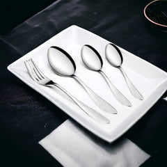 Four-piece cutlery set including fork and spoons arranged on white plate over dark tablecloth.