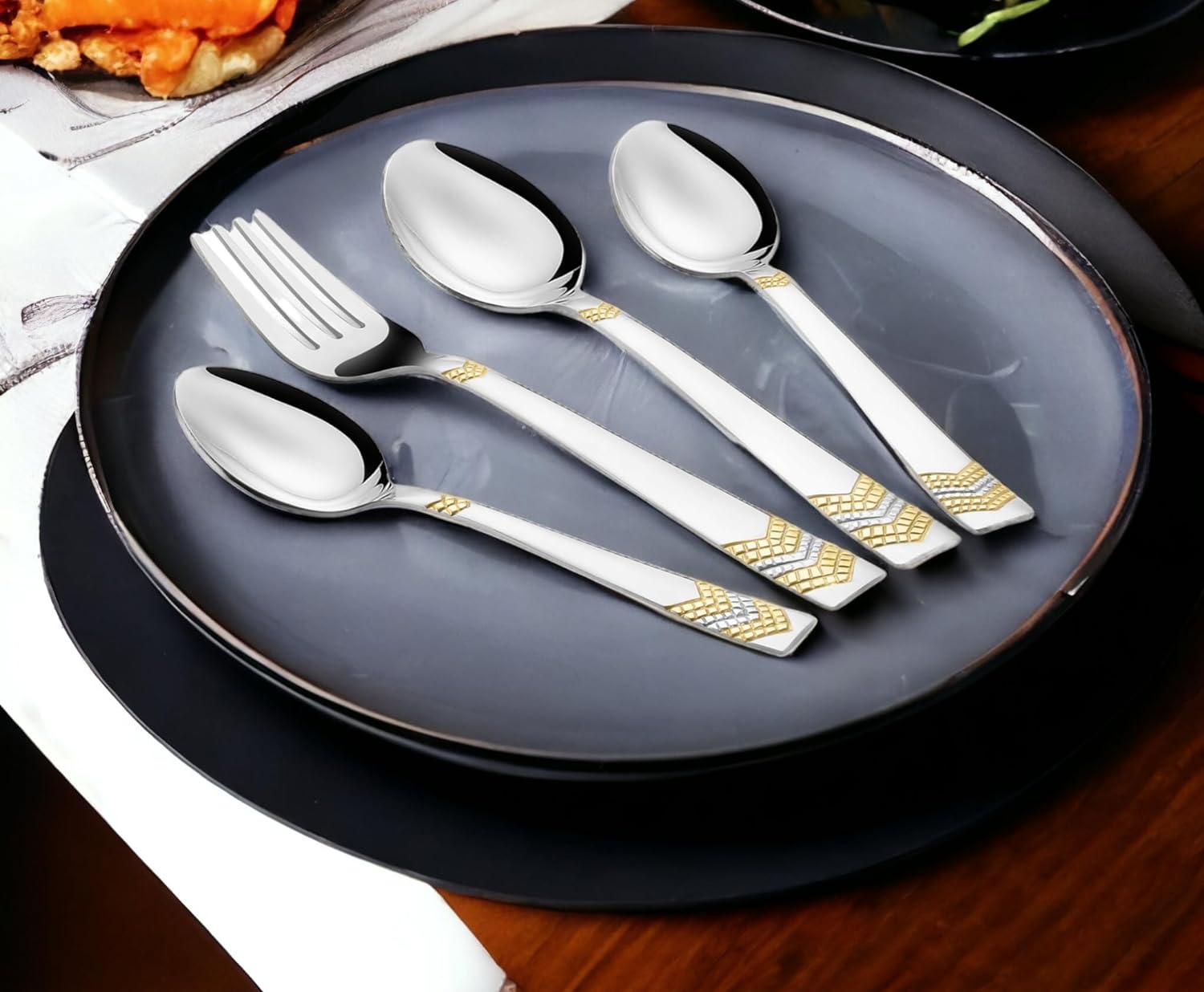 Cutlery set arranged on black ceramic plates, highlighting contrast and gold decorative handles on silverware.
