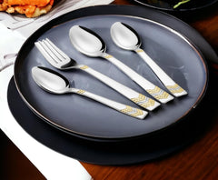 Cutlery set arranged on black ceramic plates, highlighting contrast and gold decorative handles on silverware.