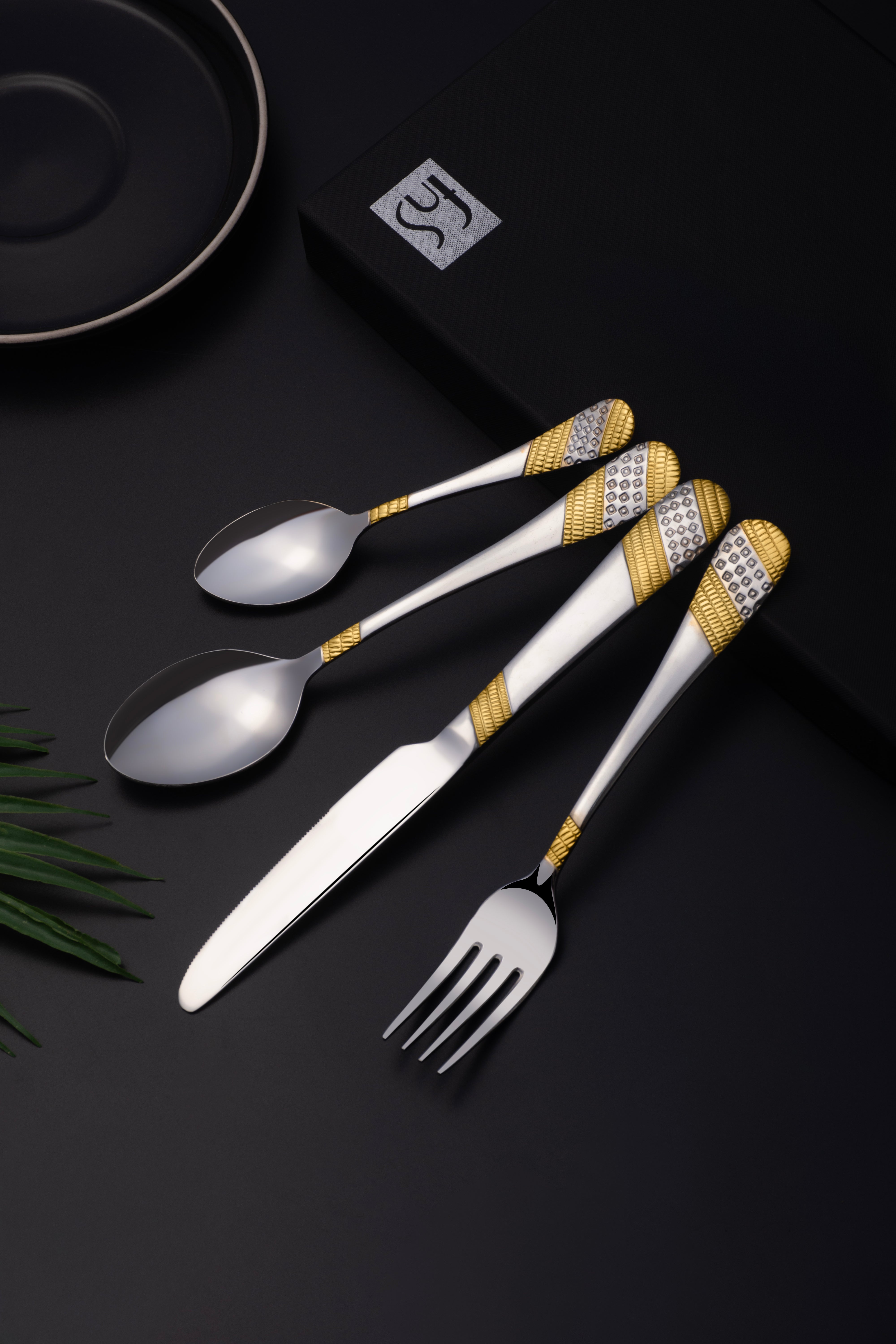 Close-up of flatware set with golden detailing placed on elegant black background near branded box.