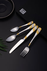 Close-up of flatware set with golden detailing placed on elegant black background near branded box.